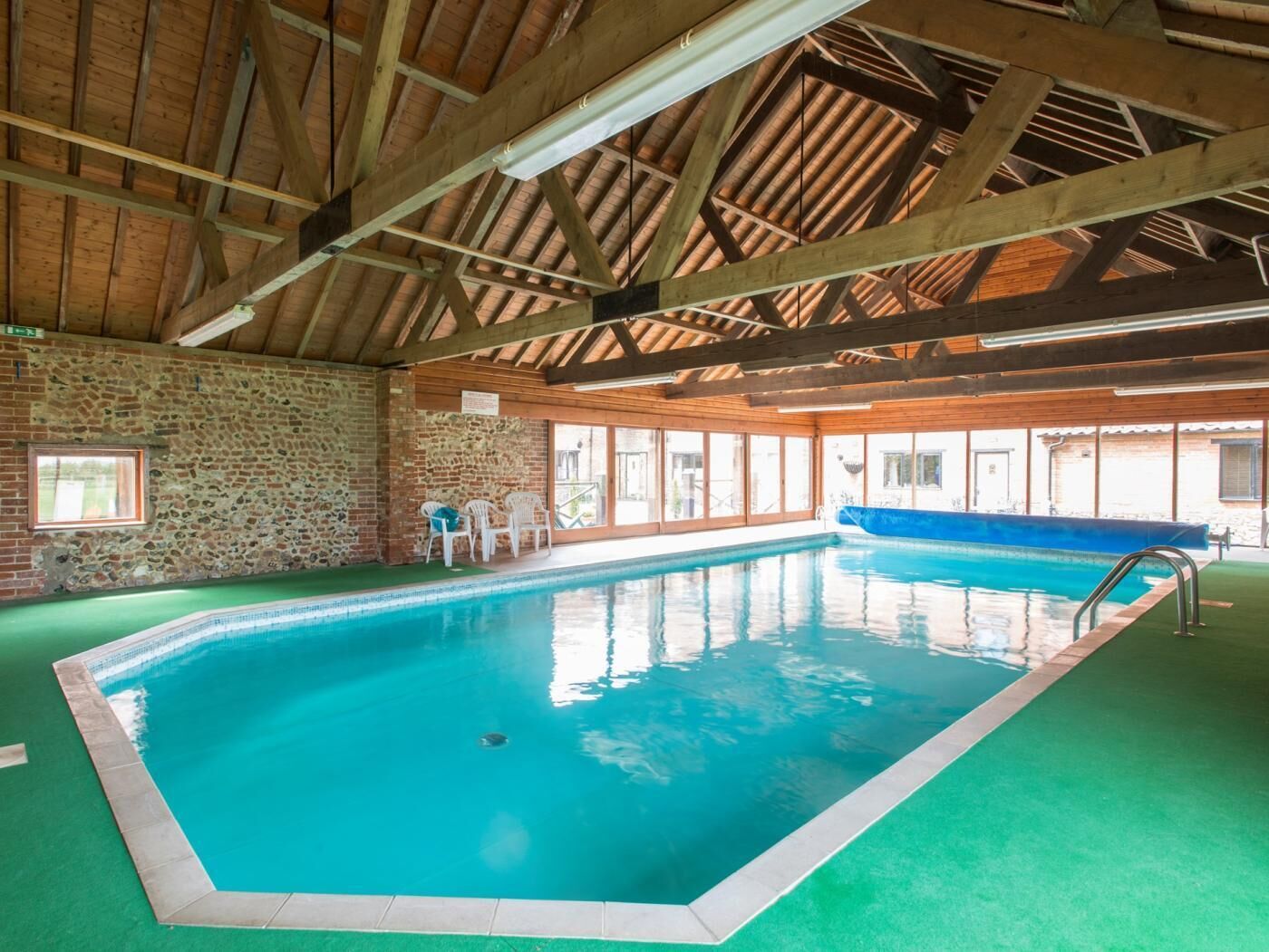 An indoor swimming pool with a stone wall, wooden beams, and a blue pool ladder.