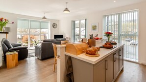 A modern kitchen with a central island, a dining area with a table and chairs, a sofa, and a TV. - 2 Bed in Haworth (oc-c37865) (Haworth)