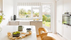 Eine moderne Küche mit Fenster, einer Spüle, einer Kaffeemaschine, einer Schüssel mit Trauben und einem Stuhl.