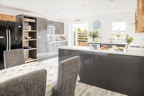A modern kitchen with a central island, built-in appliances, and a dining area with a patterned tablecloth. - 4 Bed in St. Minver (oc-l50182) (Saint Minver)