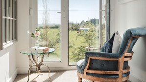Ein Balkon mit Stuhl und Tisch, Blick auf Grünflächen und Gebäude.
