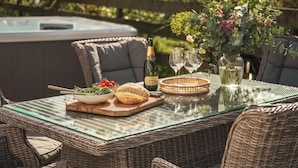 Ett bord med glasskiva, en flaska champagne, två vinglas, en skål med sallad, ett bröd och en dekorativ vas med blommor.
