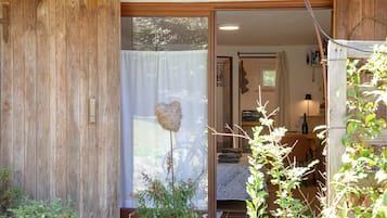 Ein Holzfassade mit einer Schiebetür, die zu einem Raum mit einem Bett, einem Fahrrad und einem kleinen Tisch mit einer Flasche führt.
