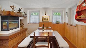 Ein Essbereich mit Holztisch, Bänken, Kamin und Fenstern mit Vorhängen.