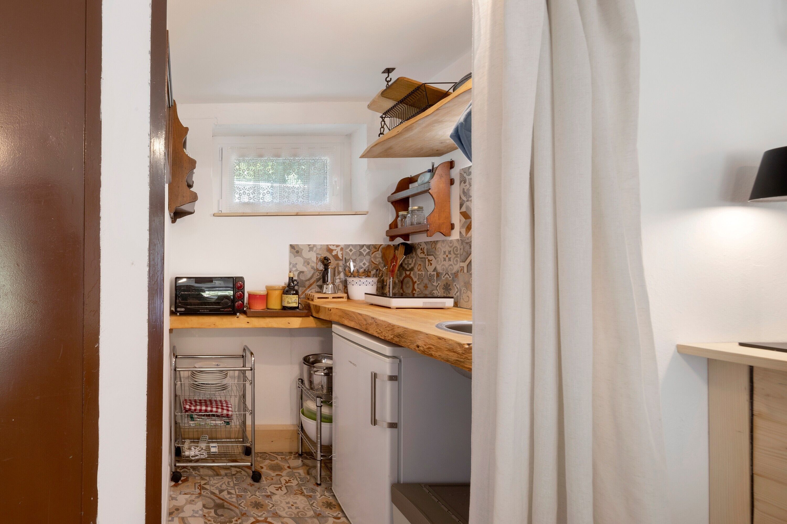 A compact kitchen with a window, a wooden countertop, a sink, and a small refrigerator.