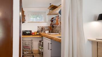 A compact kitchen with a window, a wooden countertop, a sink, and a small refrigerator.