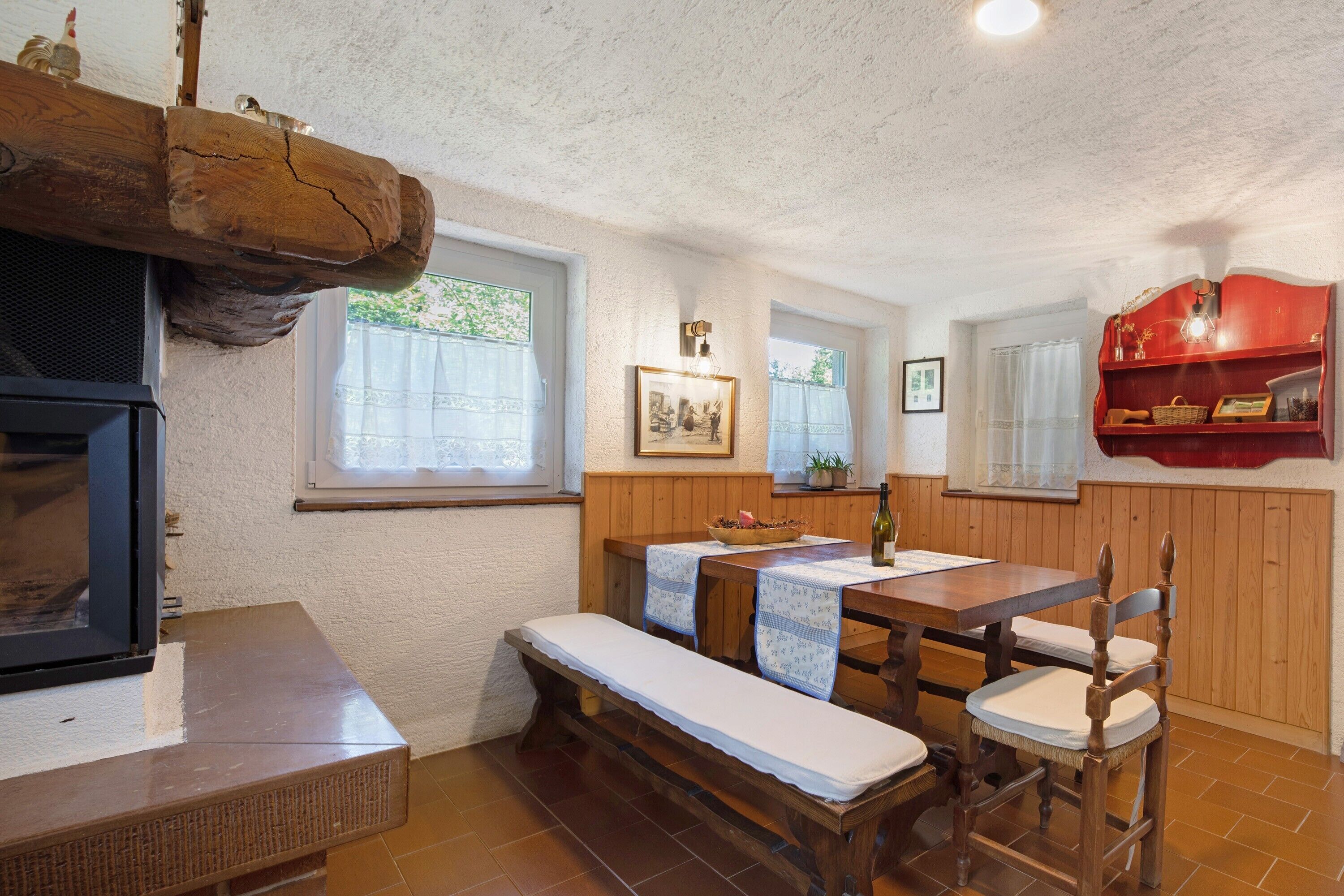A rustic kitchen with wooden furniture, a built-in stove, and a red shelf with decorative items.