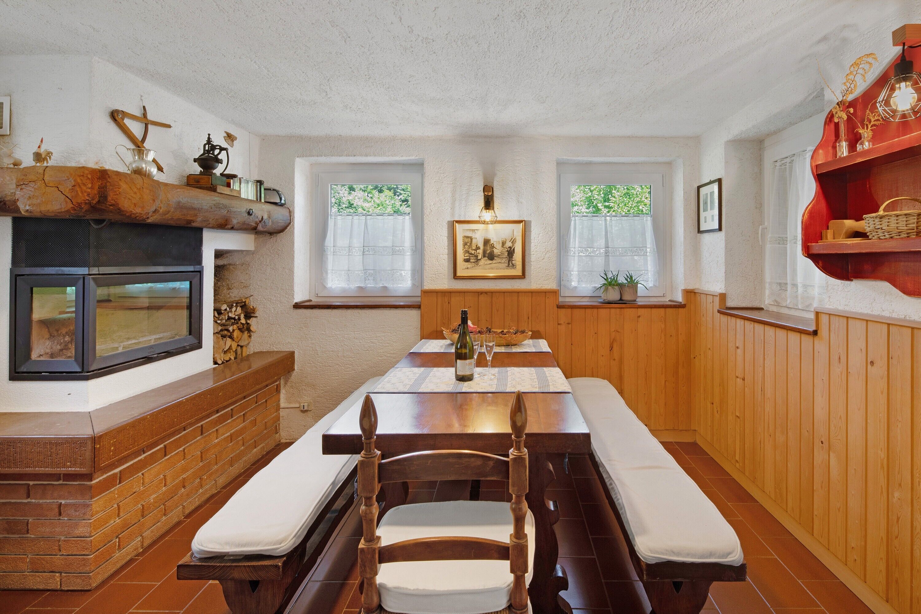 A dining area with a wooden table, benches, a fireplace, and windows with curtains.