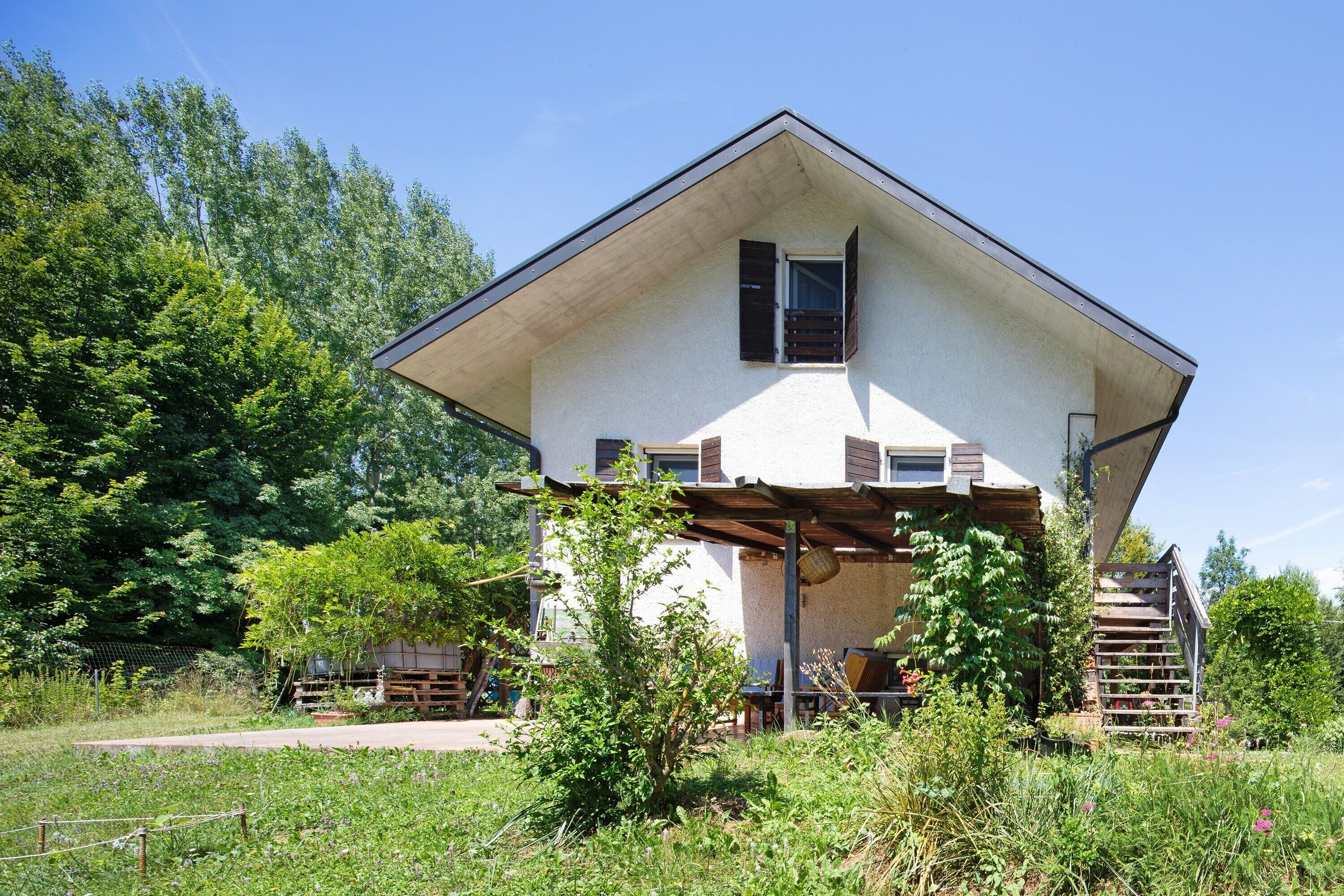 A two-story house with a sloped roof, a wooden deck, and a staircase leading to the upper floor.