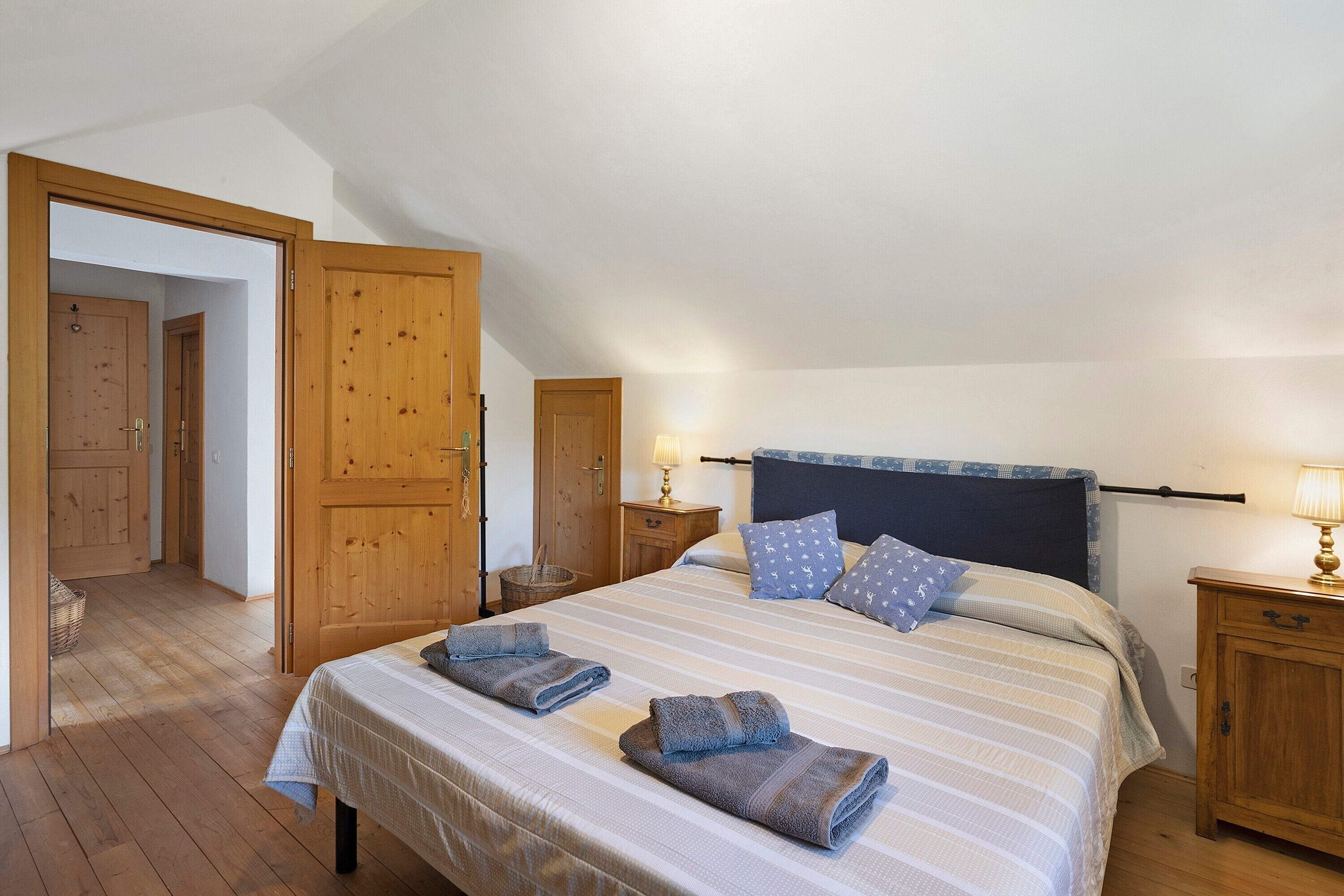 A bedroom with a bed, wooden wardrobe, and a door leading to another room.