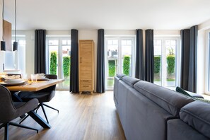 A modern living room with a sofa, dining table, and a wardrobe. - MeerNah Grömitz Apartment 6. Family-friendly. Infrared cabin. Patio (Grömitz)