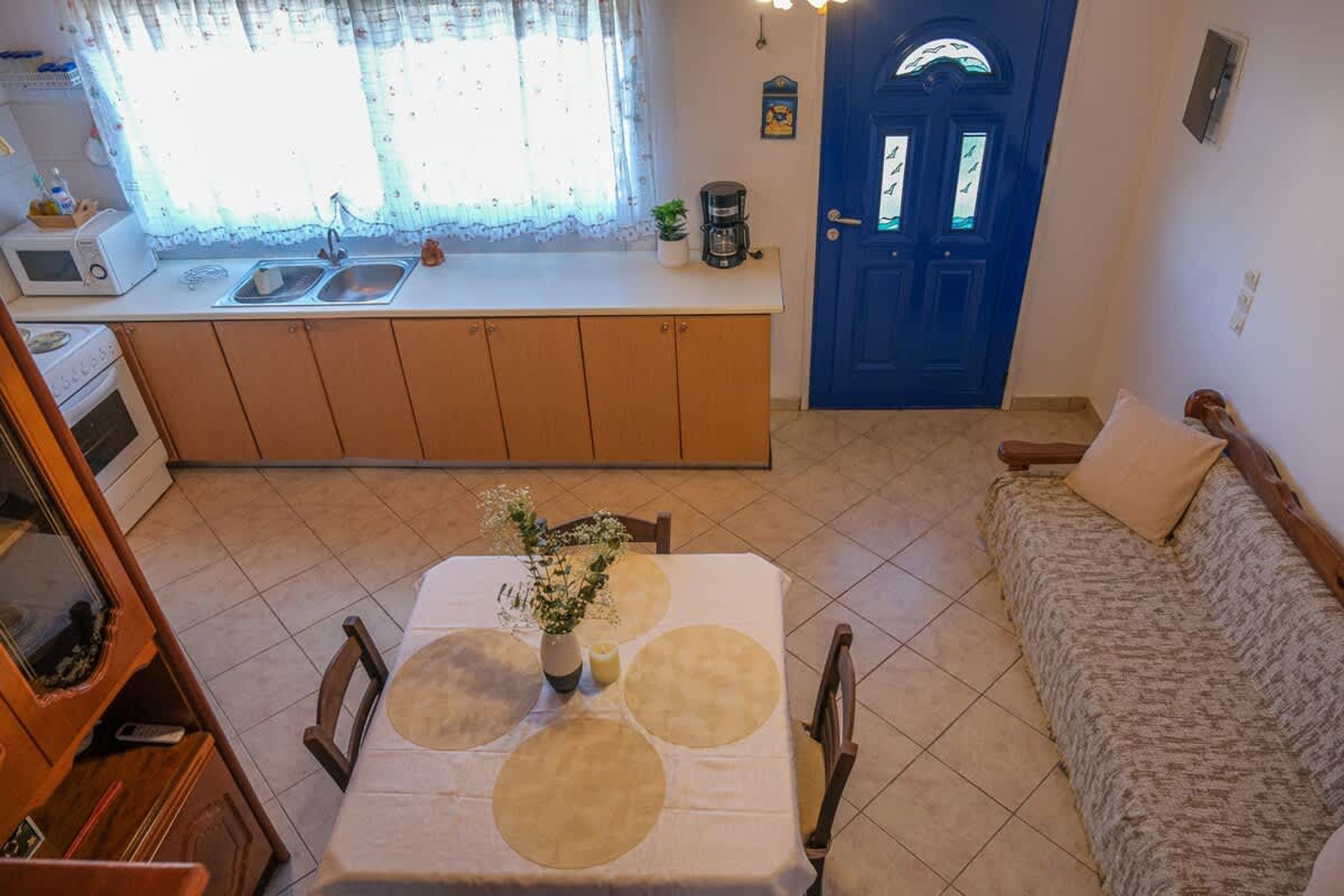 A compact living space with a kitchenette, a dining area with a table and chairs, a sofa, and a blue door.