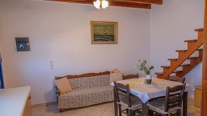 A dining area with a table, chairs, a sofa, and a staircase. - Breeze - Getaway in Samos w Serene Sea View (Samos)