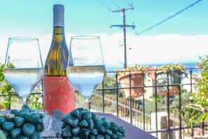 A bottle of wine and two glasses on a table with a view of the sea and buildings in the background. - Breeze - Getaway in Samos w Serene Sea View (Samos)