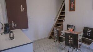 Ein kompakter Wohnbereich mit einer Küchenzeile, einer Essecke mit zwei Stühlen, einer Treppe und einem gerahmten Blumenbild an der Wand.