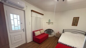 Ein Schlafzimmer mit einem roten Sofa, einem Bett, einem Heizkörper, einem kleinen Tisch und einer weißen Tür.