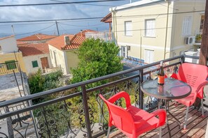 A balcony with a table and chairs, overlooking a residential area with buildings and a tree. - Little Nest in Koumeika Samou (Samos)
