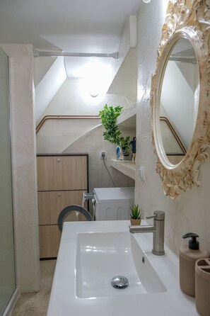 A bathroom with a white sink, a mirror with an ornate frame, a towel rack, and a potted plant. - Little Nest in Koumeika Samou (Samos)