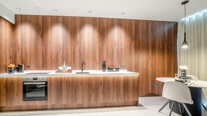 A modern kitchen with wooden paneling, a built-in oven, a sink, and a dining area with a table and chair. - 1 Bed in Oban (oc-t41733) (Achacha)