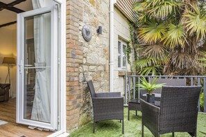 Une terrasse avec des meubles en osier, un mur en pierre et une horloge.