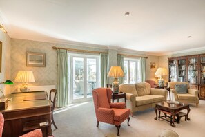 A well-lit living room with a sofa, armchairs, a coffee table, and a bookshelf. - 4 Bed in Beadnell (oc-t41388) (Beadnell)