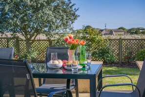 An outdoor dining table with chairs, a bowl of fruit, a vase with flowers, and bottles of water. - 4 Bed in Beadnell (oc-t41388) (Beadnell)