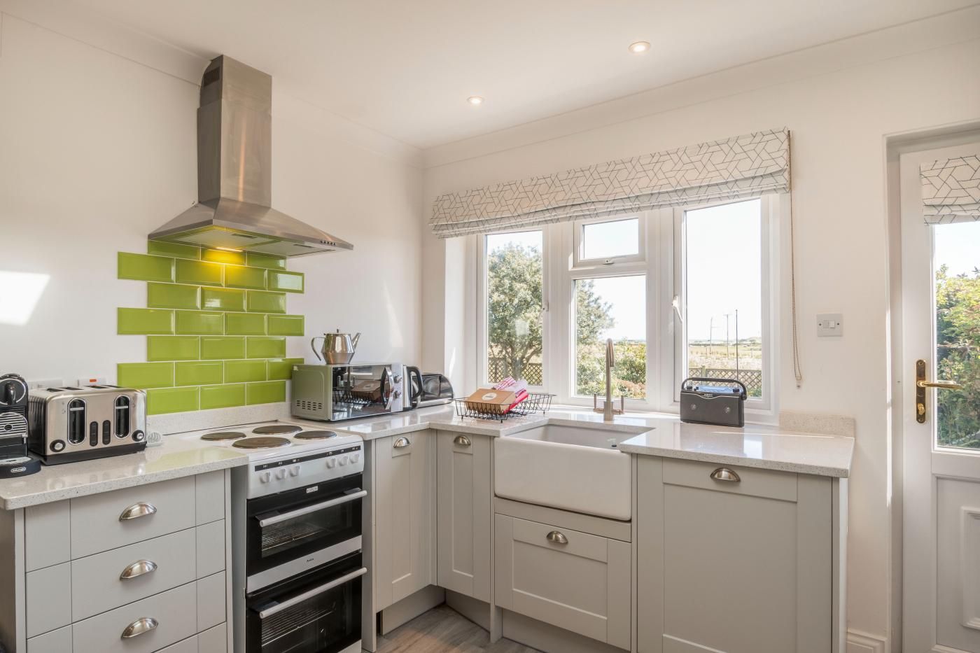 A modern kitchen with a gas stove, toaster, and oven, a window with a view of greenery, and a white door.