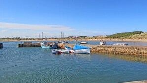 Een rustige haven met aangemeerde boten, een stenen muur en een zandstrand in de verte.