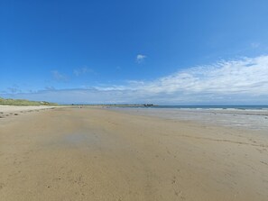 A wide sandy beach with footprints, a clear sky, and distant dunes. - 4 Bed in Beadnell (oc-t41388) (Beadnell)