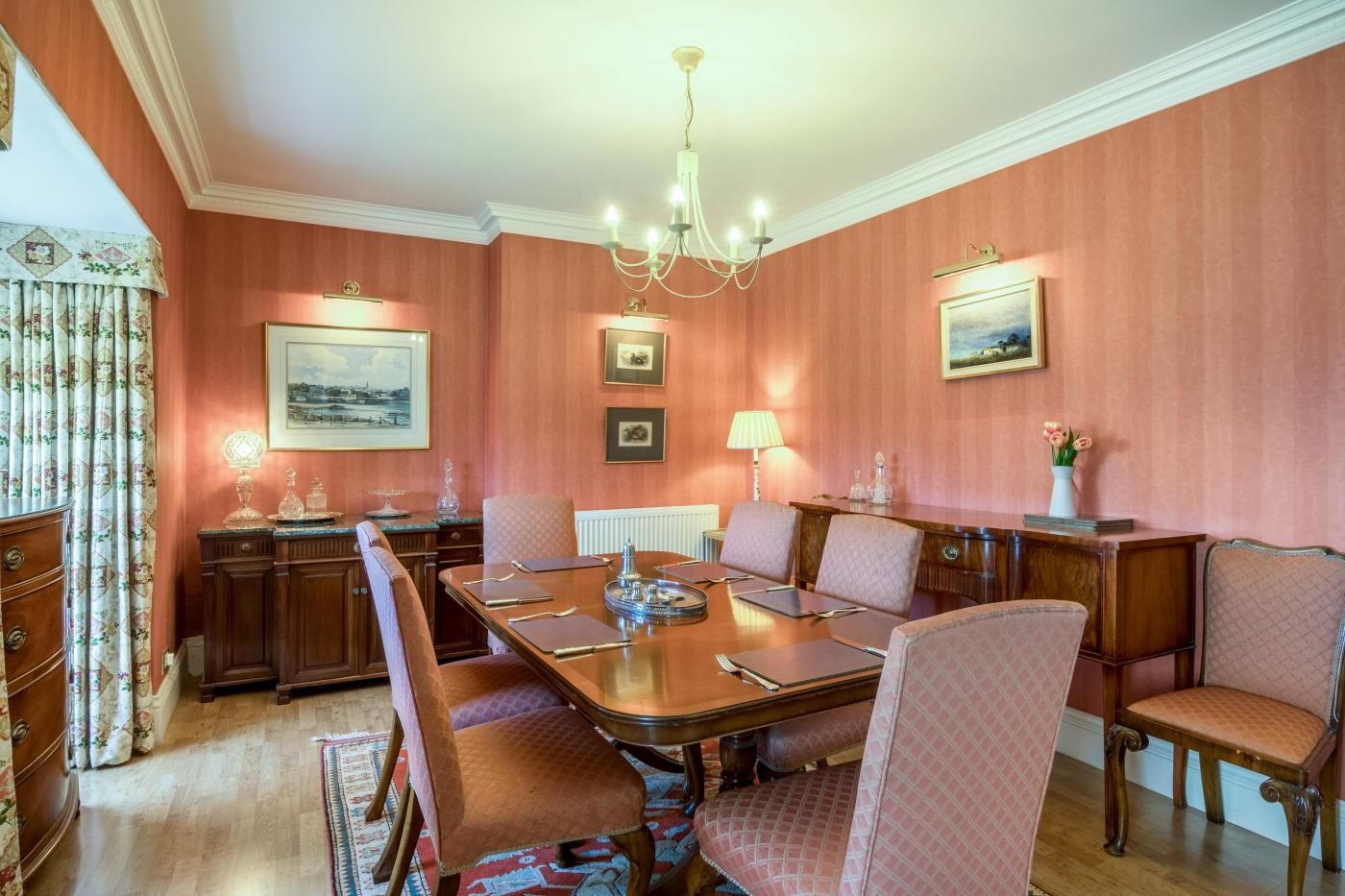 A formal dining room with a large table, chairs, a chandelier, and wall-mounted artwork.