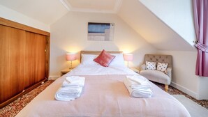 A hotel room with a large bed, two bedside lamps, a small painting, a wooden wardrobe, and a chair with a cushion. - 2 Bed in Dalrymple (oc-b40270) (Dalrymple)