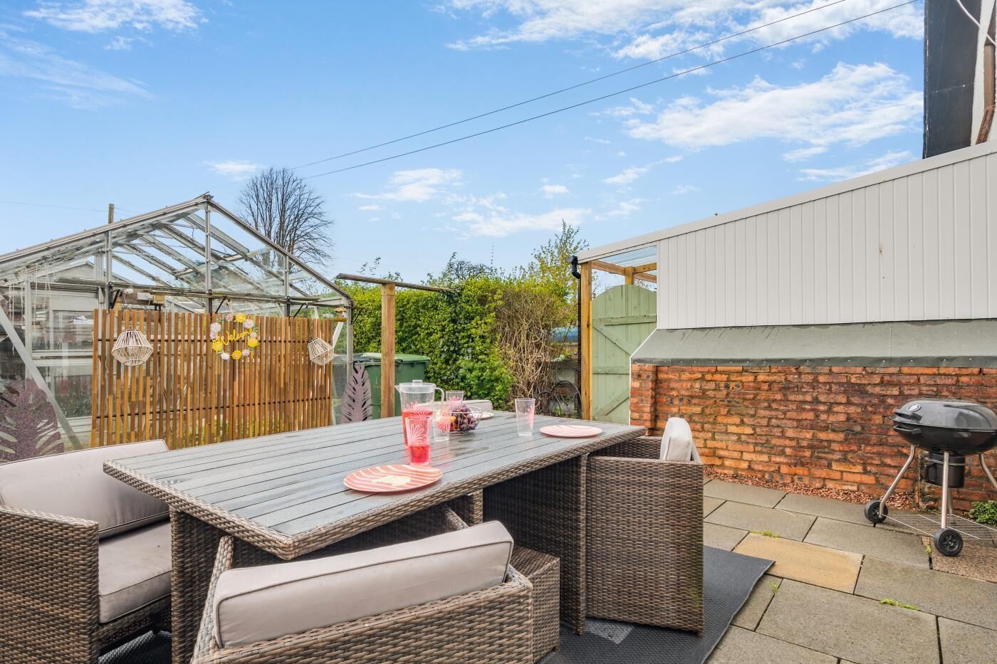 A patio with a table and chairs, a barbecue grill, and a greenhouse.