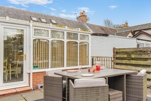 A covered patio area with a table and chairs, a glass door with a sign, and a brick wall. - 2 Bed in Dalrymple (oc-b40270) (Dalrymple)