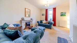 A living room with a fireplace, a blue sofa, a second seating area, and a window with red curtains. - 2 Bed in Dalrymple (oc-b40270) (Dalrymple)