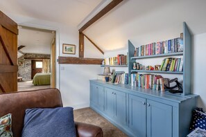 A cozy room with a bookshelf, a brown leather sofa, and a stone wall. - 2 Bed in Dulverton (oc-h34793) (Brushford)