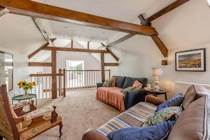 A cozy living room with a high ceiling, exposed wooden beams, a sofa set, a small table with a vase of sunflowers, and a view through a glass door. - 2 Bed in Dulverton (oc-h34793) (Brushford)