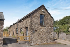 A stone building with a gabled roof, a wooden bench in front, and a sign indicating a nearby attraction. - 2 Bed in Dulverton (oc-h34793) (Brushford)