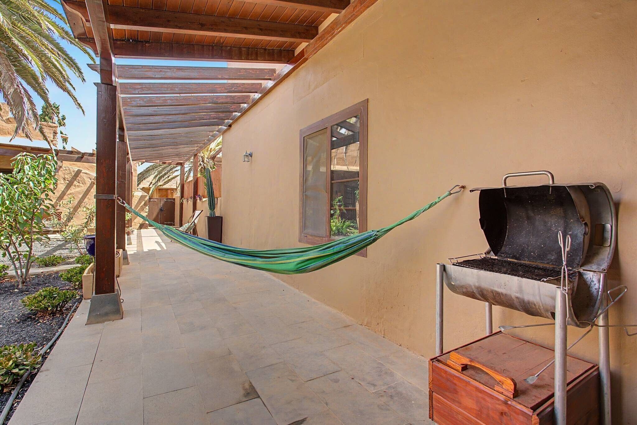Zona exterior coberta amb una barbacoa, una cadira espanyola i un camí cap a un edifici.