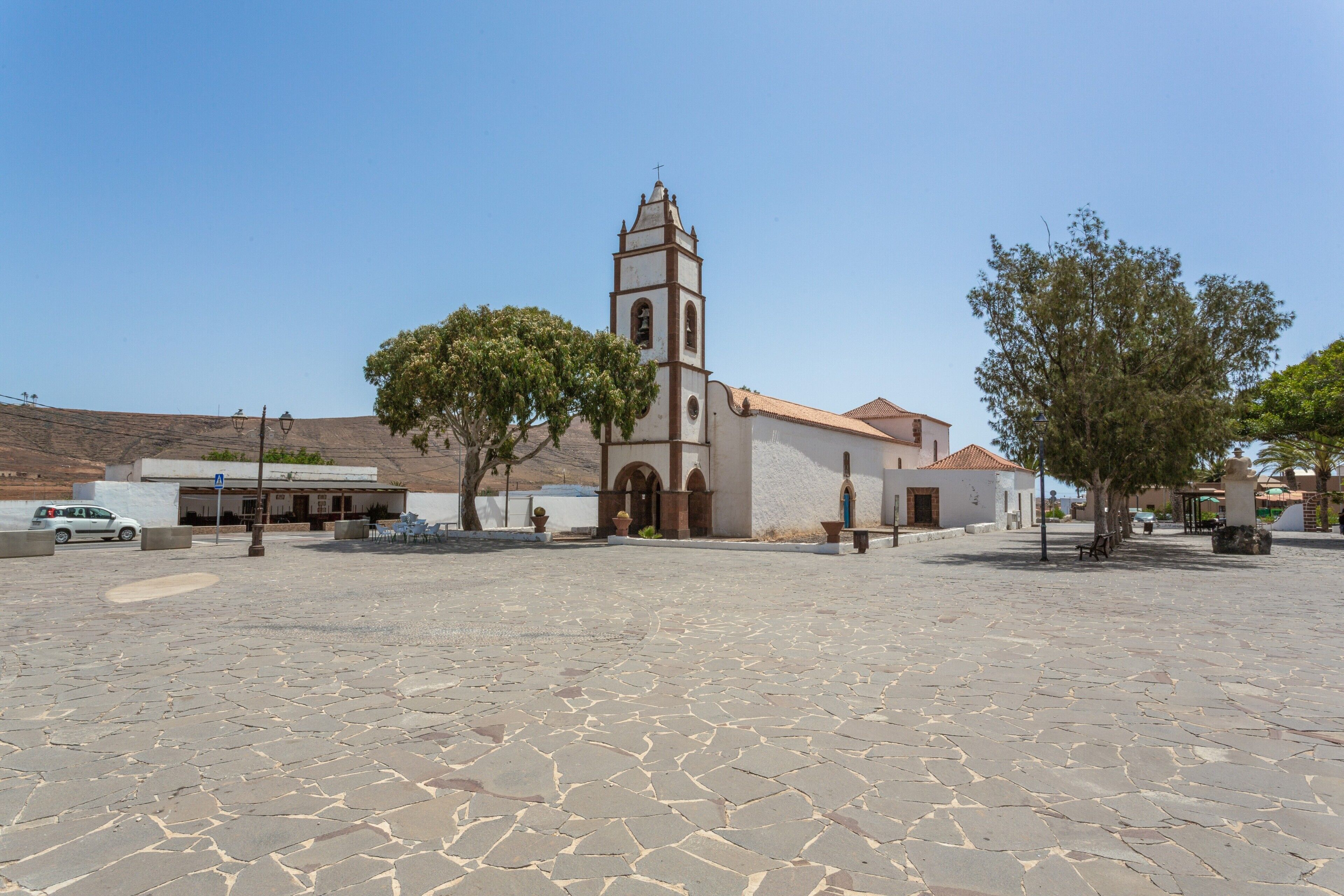 Eine Kirche mit Glockenturm, gepflastertem Innenhof und umliegenden Bäumen.