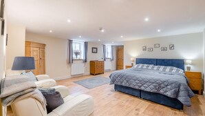 Un dormitorio con cama, mesitas de noche, cómoda, ventana con cortinas, radiador y armario de madera.