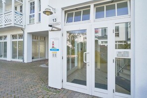 A white building with a number 13 sign, a glass door entrance, and a balcony with a white railing. - Gemutliche Ferienwohnung an der Ostsee (Sellin)