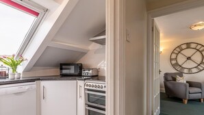 A compact kitchen with a microwave, toaster, and oven, a window with a view, and a clock on the wall. - 3 Bed in Braunton (oc-87112) (Croyde)