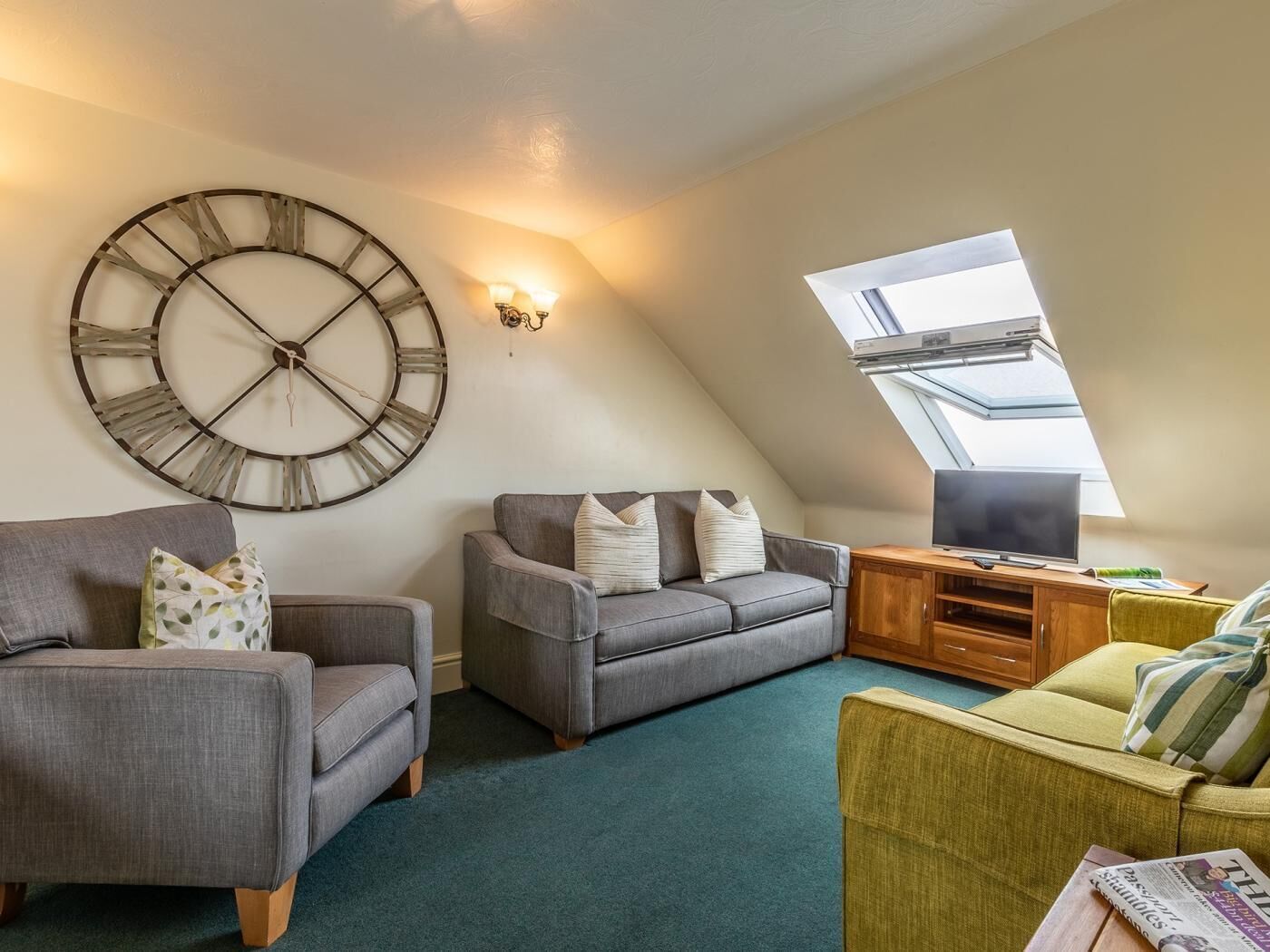 Ein Loft-Wohnzimmer mit einer großen Wanduhr, einem Fernseher auf einem Holzboden und einem Oberlicht.