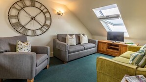 A loft-style living room with a large wall clock, a television on a wooden stand, and a skylight. - 3 Bed in Braunton (oc-87112) (Croyde)