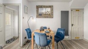 A dining area with a wooden table, four blue chairs, a wall-mounted mirror, and a radiator. - 2 Bed in Warkworth (oc-coq103) (Warkworth)
