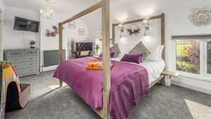 A modern bedroom with a four-poster bed, a grey dresser, a TV on the wall, and a window with a view of greenery. - 2 Bed in Warkworth (oc-coq103) (Warkworth)