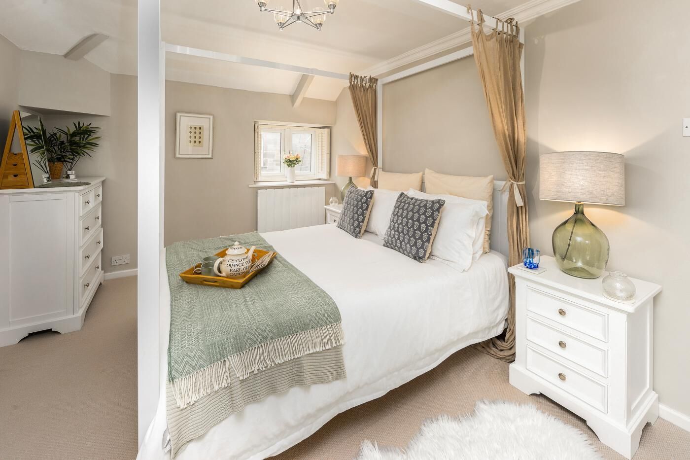 A bedroom with a canopy bed, bedside tables, a lamp, and a dresser.