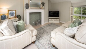 A living room with two beige sofas, a fireplace, a TV, and a window with blinds. - 2 Bed in Warkworth (oc-coq123) (Warkworth)