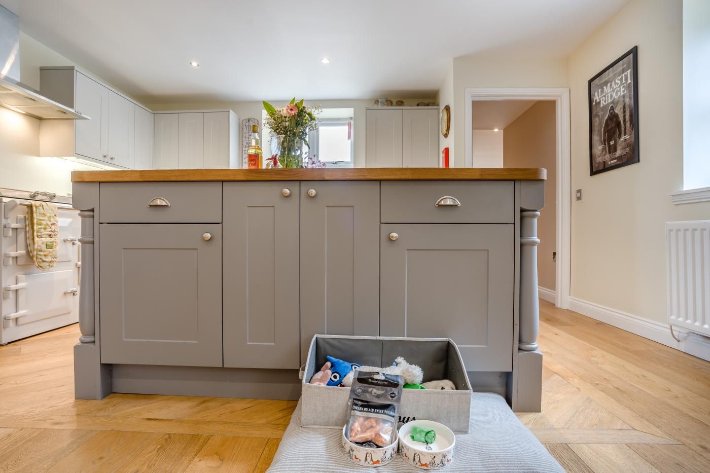 A modern kitchen with grey cabinets, a wooden countertop, and a central island with storage bins containing food items.