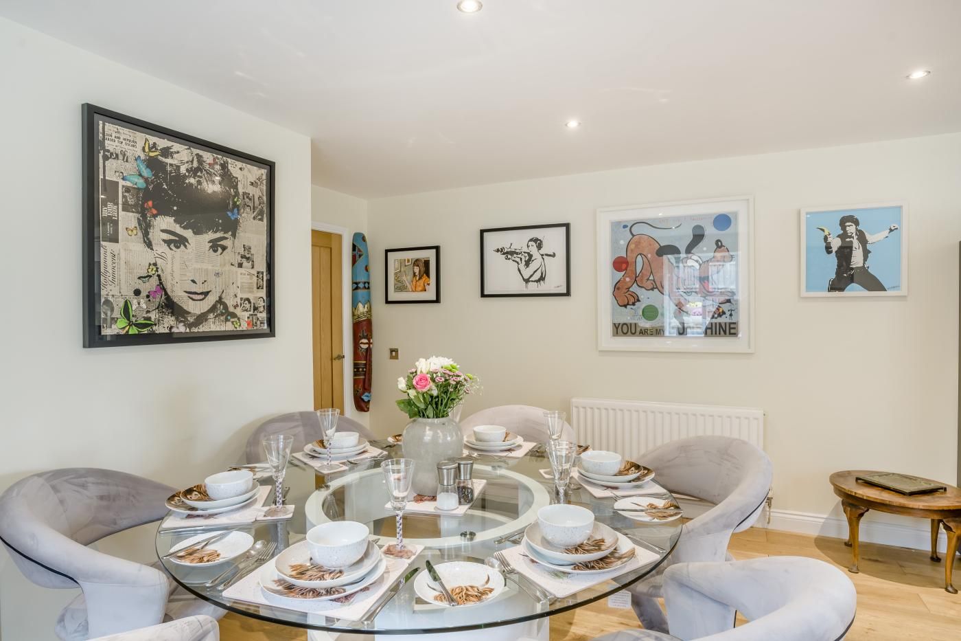 A dining area with a round glass table set for four, surrounded by grey upholstered chairs.